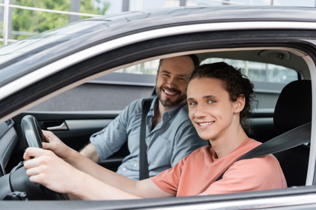 cheerful father and teenage son looking at camera while sitting together in car