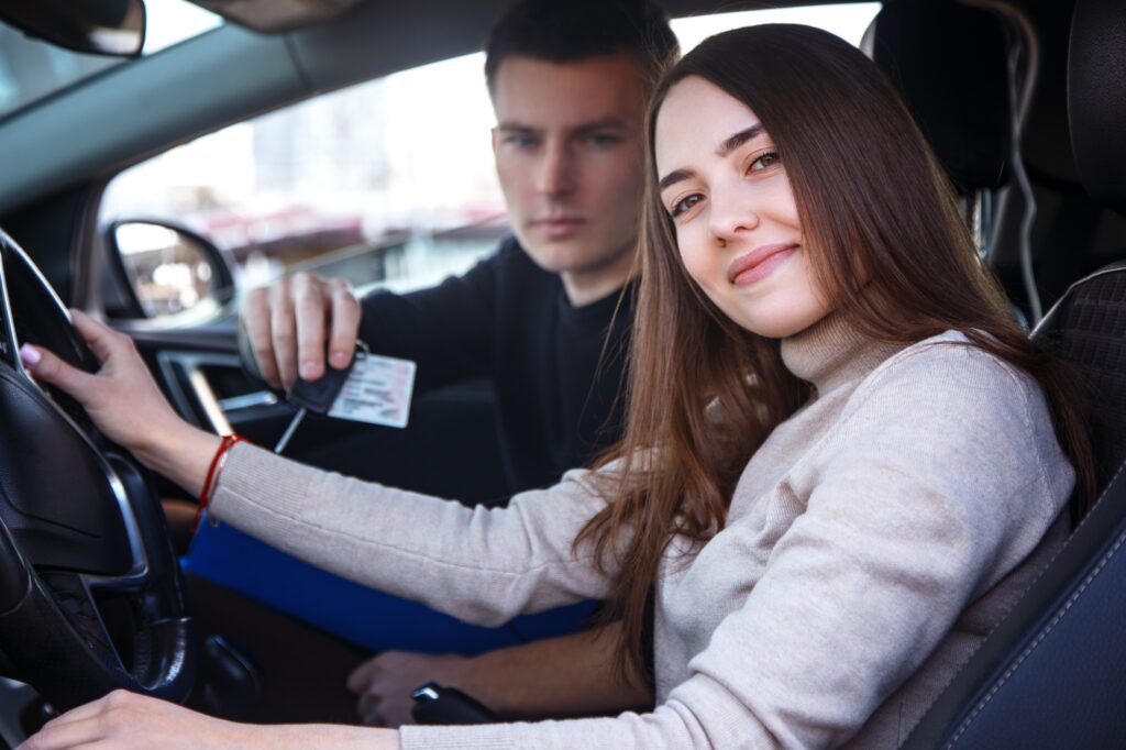 Happy girl in a new car receives a drivers license and keys from a young man.