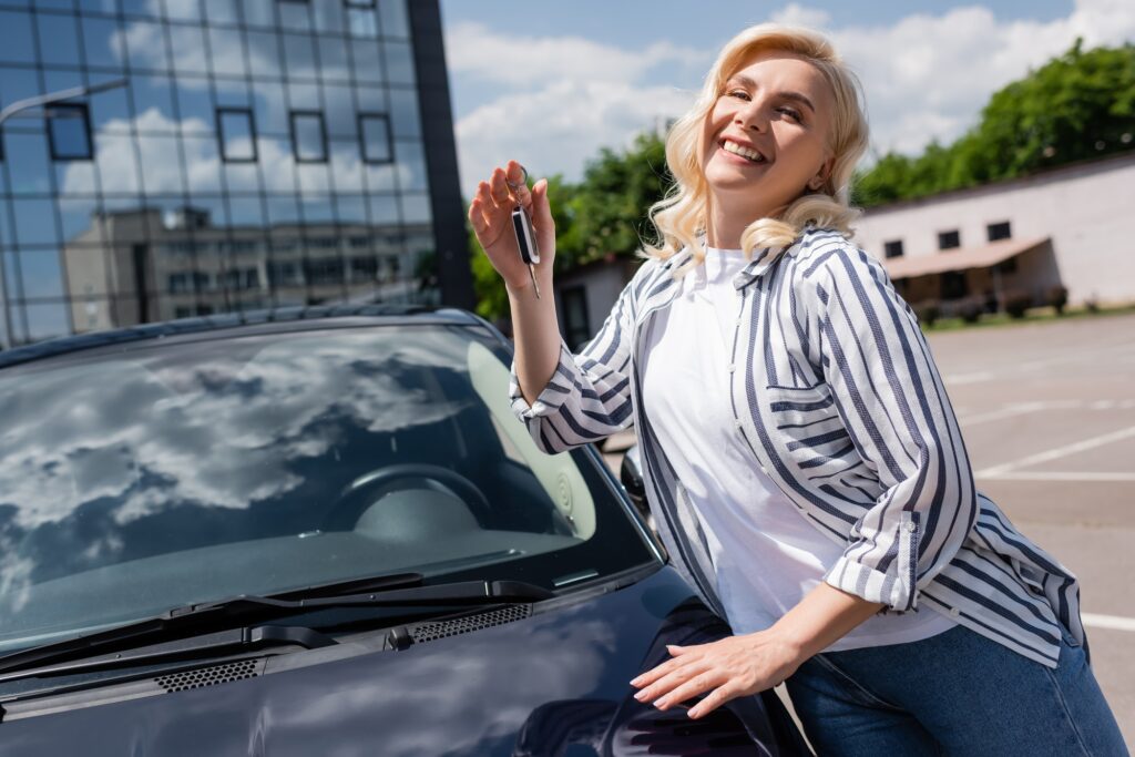 Positive blonde driver holding key near auto on urban street