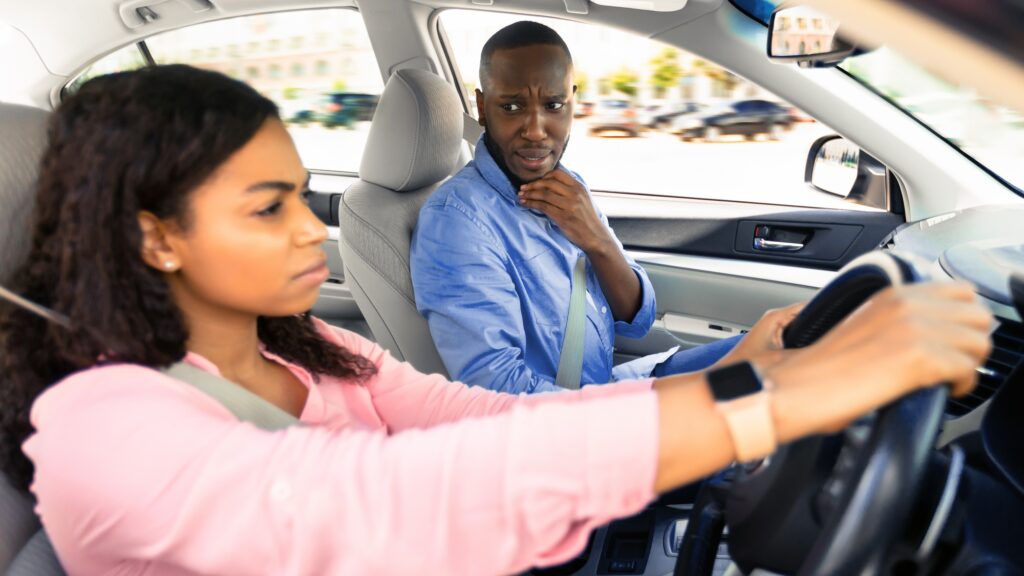 Scared instructor looking at serious focused black lady driver